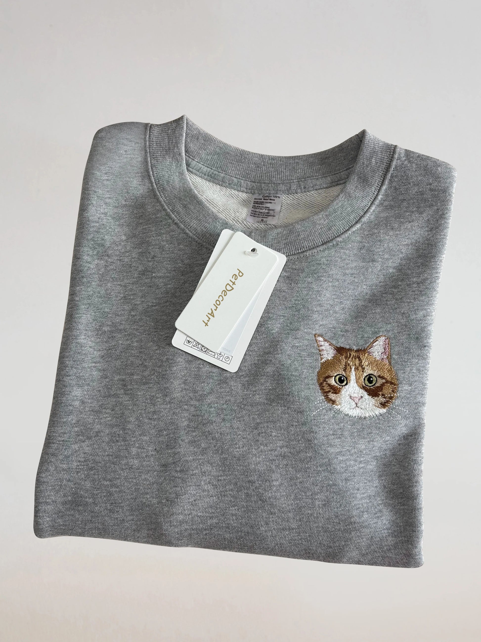 Folded grey embroidered sweatshirt showing cat face close-up