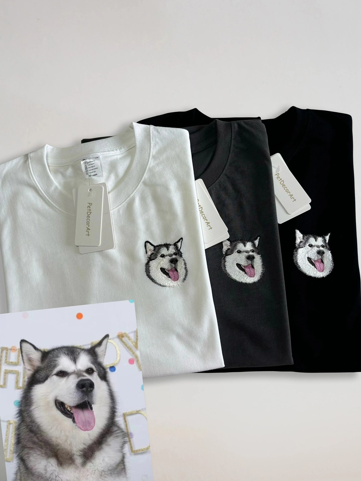 Custom embroidered dog portrait shown on white, gray, and black cotton T-shirts beside the reference photo